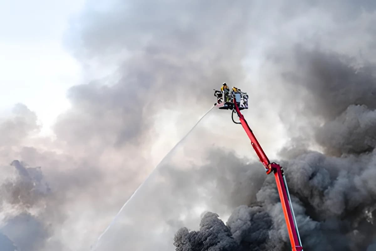 Firefighters spraying water from elevated platform amidst dense smoke