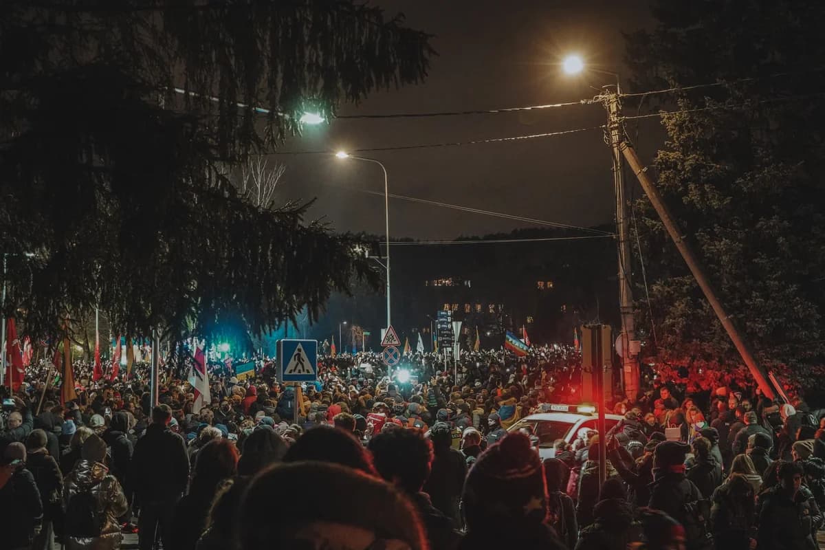 Crowded nighttime street protest with flags and police lights